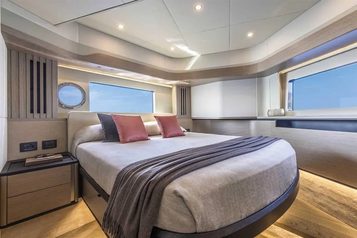 Modern yacht bedroom with a king-sized bed, grey blanket, and orange cushions, featuring large windows and stylish wooden decor.